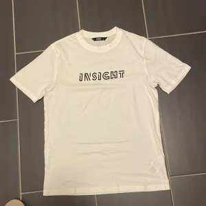 Vit t-shirt från Xside med tryck - Vit t-shirt från Xside med svart texttryck 'INSIGHT' på bröstet. Klassisk rund halsringning och korta ärmar. Perfekt basic-plagg med en clean look och skön passform.