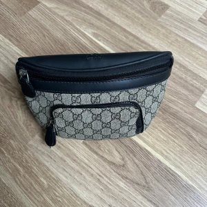 Hm beige magväska med GG-mönster - Snygg axelväska från H&M i beige och svart med klassiskt GG-mönster. Väskan har svarta detaljer i skinn, finns även flera fack med dragkedja. Perfekt för att bära det viktigaste och ge din outfit en lyxig touch.