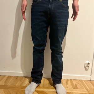 Levi's 511 Jeans - Snygga Levi's 511 jeans i mörkblå tvätt med klassisk femficksdesign och smal passform. Jeansen har guldfärgade sömmar, läderpatch bak och röd Levi's-tag på bakfickan. Perfekta för dig som gillar en modern och stilren look.