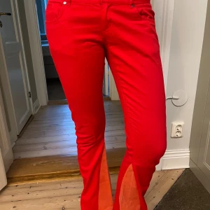 Röda bootcut jeans - Fina röda jeans, utsydda med korall tyg. Har själv sytt ut dem. Jättecoola och bra kvalitet. Ursprungligen från outfitters nation. Lite sliten lapp baktill även lite slitna nertill vid fötterna men annars utan defekter. Mått: midjemått 37 cm innerbenslängd 86 cm. Passar ca 36-38. 