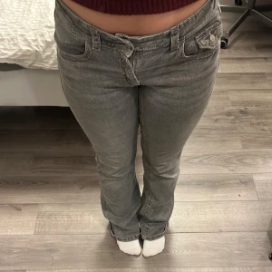 Gråa lågmidjade jeans - Säljer ett par gråa lågmidjade jeans från Gina Young. I bra skick men har några små hål längst ner på byxorna därav billigare pris.