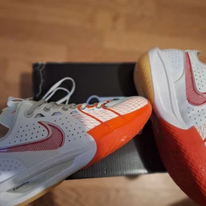 Nike Zoom sneakers vit/röd/orange - Nike Zoom sneakers med vit ovandel, röda och orange detaljer samt perforerat meshmaterial. Snyggt röd Swoosh på sidan och färgglad sula i orange och gult. Låg modell med snörning, perfekt för dig som gillar sportig och modern stil.