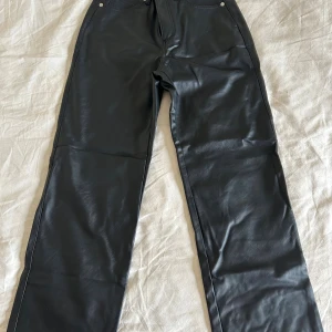 Svarta skinnbyxor från H&M, strl 36 - Snygga svarta byxor i skinnimitation från H&M i storlek 36. Byxorna har raka ben. Materialet är mjukt och följsamt. Nypris:379 kr