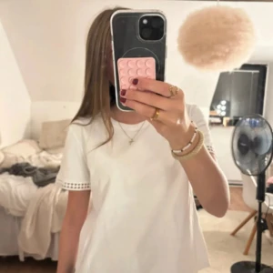 Vit t-shirt med spetsdetalj - Vit t-shirt i bomull med korta ärmar och snygg spetsdetalj längst ut på ärmsluten. Enkel och fräsch modell med rund halsringning, lånade bilder!