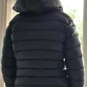 Svart Colmar dunjacka med huva - Säljer en svart dunjacka från Colmar med huva och snyggt quiltad design. Jackan har dragkedja framtill, två fickor med dragkedja och Colmar-logga på ärmen. Perfekt förkalla dagar och har en clean, sportig look. Jackan är köpt förra vintern och använd ett par enstaka gånger. Så den är i felfritt skick som ny. 
