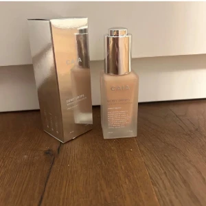 CAIA Dewy Drops Serum Foundation 20C - CAIA Dewy Drops Serum Foundation i nyansen 20C. Kommer i en frostad glasflaska med silvrig pump och lock. Innehåller 30 ml och är berikad med vitamin E och glycerin för återfuktning och lyster. Ger en naturlig, dewy finish och smälter in snyggt i huden. Helt oanvänd