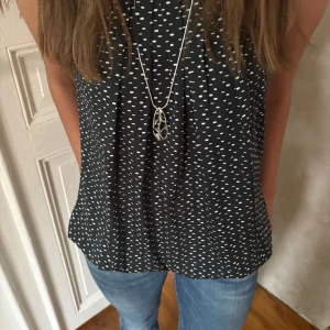 Svart prickig ärmlös blus - Säljer en svart ärmlös blus med vita prickar. Toppen har en lös passform och rund halsringning, perfekt till jeans eller kjol. Materialet känns lätt och luftigt, vilket gör den skön att bära under varmare dagar.