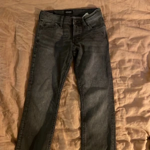 Svarta jeans från Jack & Jones - Säljer ett par svarta jeans från Jack & Jones med klassisk femficksdesign och snygga sömmar på bakfickorna. Jeansen har en rak passform och är tillverkade i ett mjukt bomullsmaterial med lite stretch för extra komfort.