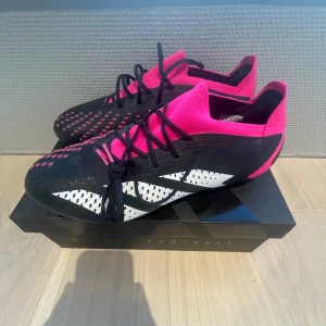 Adidas Predators  - Säljer ett par Adidas predators i storlek 42 med snygg design i svart, rosa och vit. Skorna har snörning, mönstrade detaljer och en platt sula med dobbar. Ovandelen har små taggar som ökar skruven på dina skott med rosa strumpa för skön passform. Helt oanvända och är som nya utan prislapp. Pris kan diskuteras.