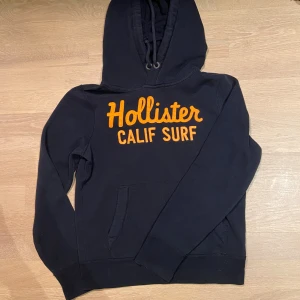 Hollister hoodie - Säljer nu en riktigt fet Hollister hoodie till ett SJUKT bra pris. Navy blå hoodie med orange skrift i storleken S perfekt till senhösten och vintern. Mitt pris endast 449 kr. Tveka inte på att kontakta mig vid minsta fundering.