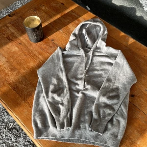 Grå hoodie med snörning - En stilren grå hoodie med huva och snörning framtill. Tröjan har långa ärmar och breda muddar vid ärmslut och nederkant. Perfekt för chill dagar och enkel att matcha med jeans eller joggers. Materialet känns mjukt och bekvämt mot huden.