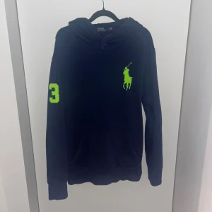 Ralph Lauren hoodie - Snygg mörkblå hoodie från Polo Ralph Lauren med stor neongrön logga på bröstet och siffran 3 på ärmen. Tröjan har huva med snörning, känguruficka och långa ärmar. Axelbredd 51cm, längd 67cm. JAG SKICKAR INGA FLER BILDER PÅ NÄR JAG BÄR PLAGGET:) 21
