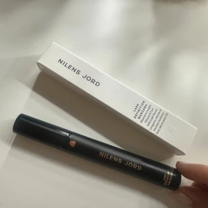 Nilens Jord Lash Definition Mascara - Snygg svart mascara från Nilens Jord med stilren tub i matt svart och guldtext. Borsten är smal och har täta strån för att ge volym och definition till fransarna. Kommer i originalförpackning. Perfekt för dig som vill ha markerade och separerade fransar.