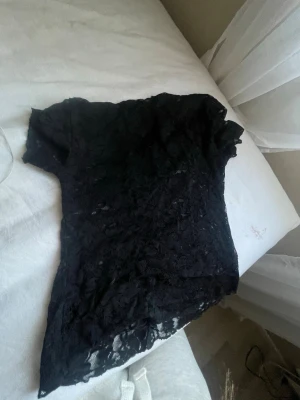 Svart spetsblus från Amisu - Snygg svart blus från Amisu i genombruten spets med korta ärmar. Perfekt att styla med jeans eller kjol för en trendig look. Blusen har en feminin passform och v-ringning framtill.