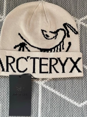 Arc’teryx Ascent Beanie – Beige – Oanvänd! -   Elegant och praktisk mössa från Arc’teryx i en tidlös beige färg. Designad med ikonisk logotyp och tillverkad av högkvalitativt, behagligt material som ger värme och komfort i både stadsmiljö och ute i naturen. Mössan är helt oanvänd och originaltaggarna sitter kvar.  Arc’teryx Ascent Beanie – Beige – Unused
