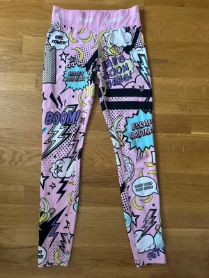 Stronger träningstights  - Träningstights från Stronger med färgglatt serietidningstryck i blått, gult, svart och vitt.                                     Jag säljer även den matchande sport-behån.  Helt nya.                                                                             Ordensrie pris: 799kr