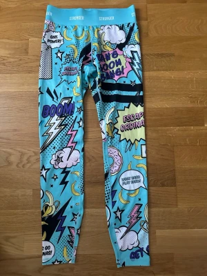 Stronger träningstights  - Träningstights från Stronger med färgglatt serietidningstryck i blått, gult, svart, vitt och rosa. Helt nya.                                                                             Ordensrie pris: 799kr
