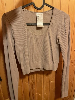 Croppad långärmad - Trendig beige croppad topp med lång ärm och rundad urringning, stretchig material. Bra att styla med höga jeans eller kjol för en snygg look.
