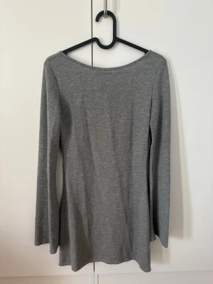 Grå långärmad klänning med öppen rygg - Snygg grå långärmad klänning med djup öppen rygg och knytband i nacken. Tillverkad i mjukt material som sitter bekvämt och har en enkel, stilren look. 