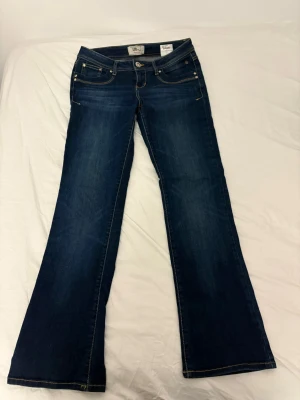 Mörkblå bootcut jeans från LTB Low waist  - Snygga mörkblå bootcut jeans från LTB med klassiska fem fickor och kontrastsömmar. Jeansen har låg midja och lätt utsvängda ben, vilket ger en retrovibe. Tillverkade i slitstark denim med subtila slitningar framtill. Storlek W28 L32