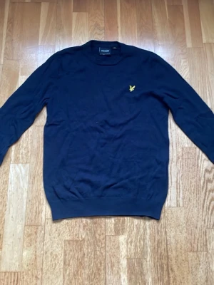 Mörkblå stickad tröja Lyle & Scott - Mörkblå stickad tröja från Lyle & Scott med klassisk rund hals och lång ärm. Den är helt ny använd 2 gånger. Tröjan har den ikoniska gula örnloggan broderad på bröstet och ribbade muddar vid ärmslut och nederkant. Tillverkad i mjukt material för en clean och stilren look. Storlek M men sitter som S, jag har själv S i storlek på allt typ och den passar mig. Hör av dig vid frågor!
