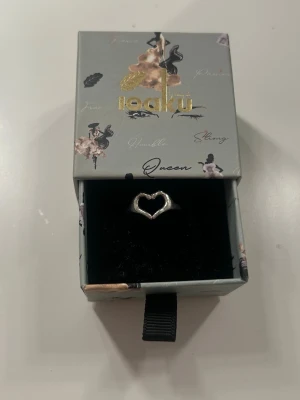 Silverring med hjärta från Ioaku - Snygg silverfärgad ring från Ioaku med ett öppet hjärta som detalj.Säljer eftersom den inte kommer till användning längre. Storleken går att justera och den är i jätte bra skick, som ny! Skriv vid frågor eller om ni vill ha fler bilder💕💕Påse och asken ingår