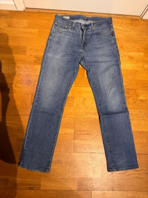 Blå raka jeans från Levi's - Klassiska blå jeans från Levi's med rak passform och fem fickor. Jeansen har en ljus tvätt och är tillverkade i bomull. Perfekta för en avslappnad och tidlös stil. DEFEKT lagning på baksidan bild 3