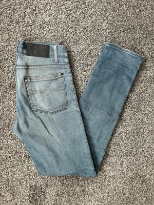 Ljusblå tiger of sweden jeans - Säljer ett par ljusblå tiger of sweden jeans med klassisk femficksdesign och diskreta slitningar framtill. Jeansen har normal midja och smala ben, perfekta till sneakers eller boots. Materialet är mjukt denim med lite stretch för extra komfort.