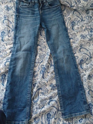 Blå bootcut jeans med broderade fickor från gina tricot  - Säljer ett par blå bootcut jeans med snygga broderade detaljer och silverknappar på bakfickorna. Klassisk femficksmodell med normal midja och slitningar framtill. Perfekta för dig som gillar en avslappnad men ändå trendig stil.