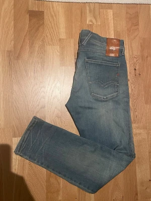 Replay anbass jeans  - Säljer ett par blå jeans från Replay med klassisk femficksmodell och raka ben. Jeansen har en snygg tvättad look med lätt slitning på låret och bakficka med Replay-läderpatch i midjan. Perfekta för en avslappnad stil.