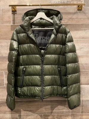 Herno jacka  - Snygg mörkgrön dunjacka från Herno med glansig finish, huva och två dragkedjeförsedda fickor. Jackan har quiltad design och raka ärmar. Perfekt för kalla dagar när du vill hålla stilen.