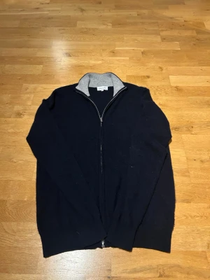 Mörkblå ziptröja från Davida - Mörkblå ziptröja från Davida Cashmere. Tröjan har hel dragkedja framtill och är tillverkad i ett mjukt material, perfekt för lager-på-lager. Enkel och stilren design som passar till många outfits.