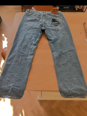 Ljusblå raka Burberry supreme jeans - Säljer ett par ljusblå jeans från Burberry/supreme med raka ben och klassisk femficksmodell. Jeansen har Burberry-logga broderad på bakfickan och är gjorda i mjuk denim. Perfekta för en avslappnad och trendig look.