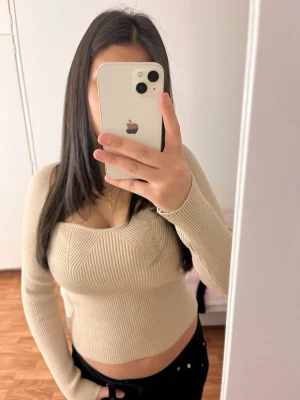 Beige ribbad långärmad topp - Trendig beige ribbad topp med lång ärm och snygg v-ringad skärning vid bysten. Figurnära passform som framhäver siluetten. Perfekt att styla med jeans eller kjol för en cool look.