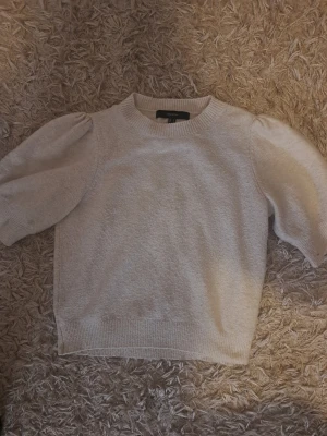 Beige stickad tröja Vero Moda - Säljer en beige stickad tröja från Vero Moda med puffärmar och rund halsringning. Tröjan har ribbade muddar vid ärmslut och nederkant, och är gjord i ett mjukt material. Perfekt för dig som gillar en enkel men trendig look. 