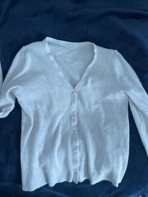 Vit ribbad kofta med knappar - Säljer en vit ribbad kofta med v-ringning och långa ärmar. Osäker på storlek men är nog XS