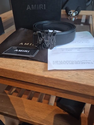 Svart läderbälte från Amiri - Snyggt svart bälte i läder från Amiri med en stor, cool metallspänne i form av Amiris logotyp. Bältet har stilrena sömmar och levereras med originalförpackning, dustbag och certifikat. Perfekt accessoar för att lyfta din outfit. 110cm