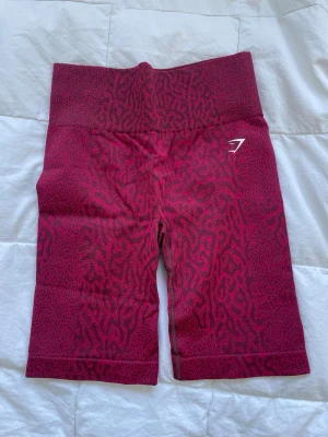 Röda mönstrade shorts Gymshark - Snygga högmidjade shorts från Gymshark i rött med animalprint. Stretchigt material som sitter tight och bekvämt, perfekt för träning. Diskret logga framtill och scrunch-detalj bak för extra passform.