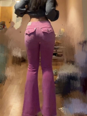 Rosa bootcut jeans från true religion  - Säljer ett par rosa bootcut jeans från Juicy Couture med fickor bak som har lock och knappdetaljer. Jeansen har en utsvängd passform och är tillverkade i ett mjukt material som ger en skön retrovibe. Perfekta för dig som vill sticka ut med färg!
