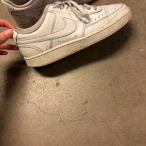 Vita Nike Air Force 1 sneakers - Klassiska vita Nike Air Force 1 sneakers i lågt snitt. Skorna har en clean design med perforerad tåbox, vita skosnören och den ikoniska swoosh-loggan på sidan. Tillverkade i läder med gummisula för skön komfort och streetstyle-vibe. Pris kan diskuteras vid snabb affär