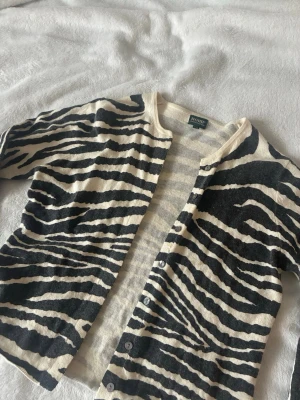 Zebramönstrad kofta från House - Snygg zebramönstrad kofta i svart och vitt. Koftan har rund halsringning, knäppning framtill och långa ärmar. Perfekt för dig som vill sticka ut med ett djurmönster. Mjuk och tunn i materialet, passar året runt.