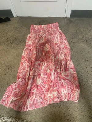 Rosa paisleymönstrad långkjol - Säljer en flowy långkjol med rosa och vita paisleymönster. Kjolen har resår i midjan för skön passform och är gjord i ett lätt material som passar perfekt till varma dagar. 