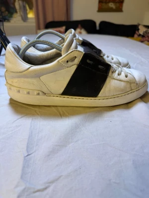 Valentino Open sneakers vita – Svarta stripes – Strl 44 – Sjukt snygga - Sjukt snygga Valentino Open sneakers i vitt med svarta stripes, storlek 44. Riktigt clean och lyxig design som funkar till exakt allt.  Perfekta för clean fit, minimal style, streetwear eller uppklädda outfits. Valentino Open är en av de mest eftertraktade designer-sneakers på marknaden.  • Märke: Valentino • Modell: Open • Färg: Vit med svarta detaljer • Storlek: 44