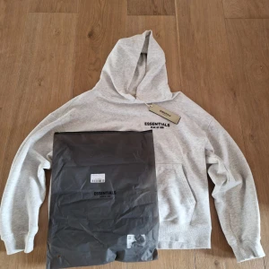 Grå Essentials hoodie med huva - Snygg ljusgrå hoodie från Essentials.  Den är storlek s men kan kännas lite större        Hör av om ni har fler frågor✅
