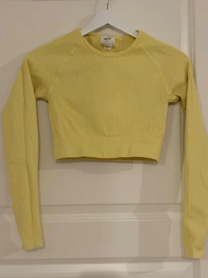 Gult ribbat träningsset Aim'n - Säljer ett gult ribbat träningsset från Aim'n med långärmad crop top och matchande tights med hög midja. Setet är gjort i stretchigt material som sitter skönt och följer kroppen. Perfekt för gymmet eller yoga, eller chilla hemma! 
