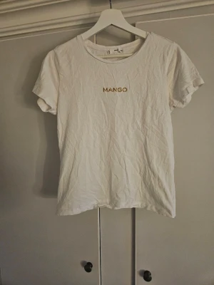 Mango T-shirt  - Vit T-shirt från mango med ett guldigt märke. Storlek L men väldigt liten i storlek, motsvarar en s/m i storlek.