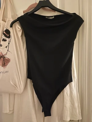 Svart body från Zara - Stilren svart body från Zara med rund halsringning och korta ärmar. Tillverkad i ett mjukt och stretchigt material som sitter snyggt på kroppen. Perfekt att matcha med jeans eller kjol för en clean look. Helt ny utan prislapp