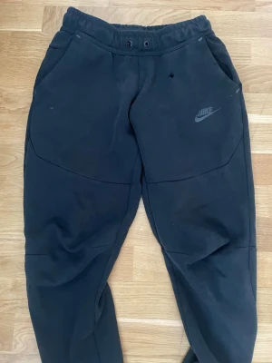 Svarta mjukisbyxor från Nike - Säljer ett par svarta mjukisbyxor från Nike med dragsko i midjan och två sidofickor. Byxorna har en avslappnad passform och Nike-logga tryckt på vänster sida. Tillverkade i mjukt bomullsmaterial, perfekta för chill dagar eller träning.