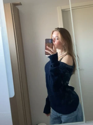 Mörkblå off shoulder stickad tröja - Mysig mörkblå stickad tröja med off shoulder-design och bred krage. Tröjan har lång ärm och är figurnära i modellen. Perfekt för dig som gillar en avslappnad men ändå trendig stil.