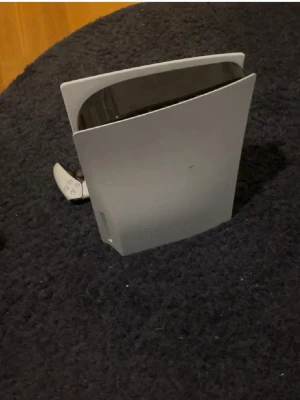 Ps5 - Säljer en PlayStation 5 konsol från Sony i vit och svart design. Konsolen har en futuristisk, böjd form och är tillverkad i plast. En trådlös DualSense-handkontroll i matchande färg ingår. Perfekt för gaming och nya spelupplevelser.